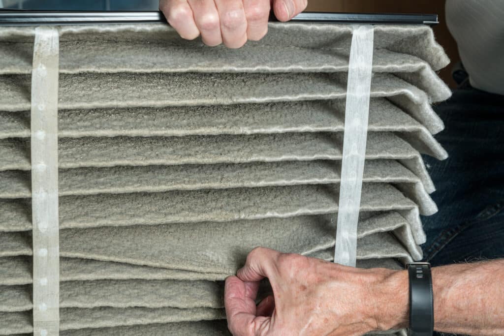 Senior caucasian man looking at the dust in folded dirty air filter in the HVAC furnace system in basement of home